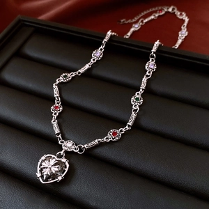 Close-up of gothic heart cross pendant with multicolored gems and silver chain links