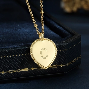 Macro view of a gold-tone heart letter C pendant on a blue velvet jewelry box