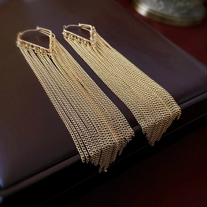 Close-up of golden long chain tassel earrings with triangular studs on leather surface