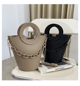 Close-up of khaki and black bucket bags with round handles and chunky chain details
