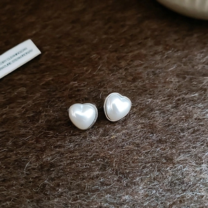 Gros plan de boucles d'oreilles cœur en perle avec bordure argentée sur tissu doux