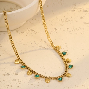 Golden stainless steel heart pendant necklace with green crystal tassels on stone surface
