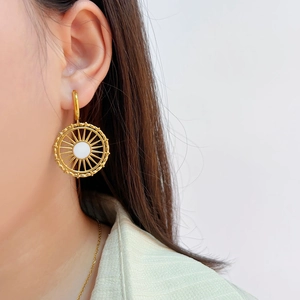 Détail de la boucle d'oreille ronde creuse dorée avec incrustation blanche sur un mannequin