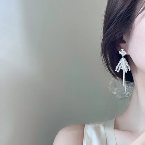Close-up of silver clover tassel earrings with clear crystal beads on a model