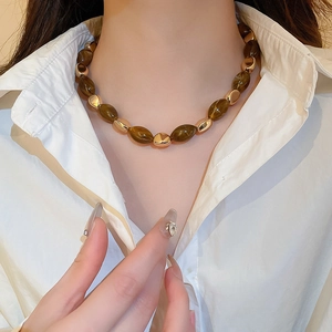Detail of necklace with dark brown resin oval beads and golden metal spacers on a model