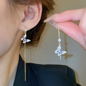 Détail de boucles d'oreilles dorées asymétriques avec papillons bleus et perles blanches