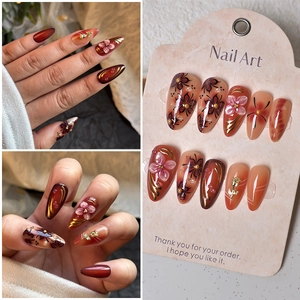 Detail of almond press-on nails with 3D pink flowers, gold relief, and cherry red gradient