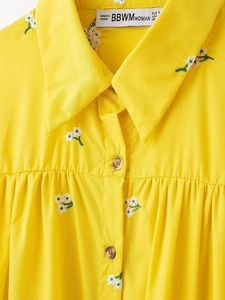 Detailed view of yellow dress with white flower embroidery, doll collar, and buttons