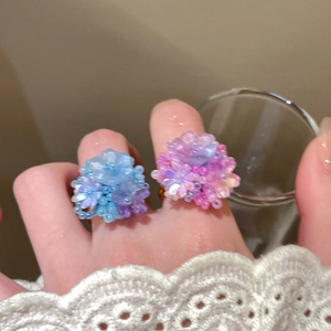 Close-up of handmade resin flower rings in pastel blue and pink on model's fingers