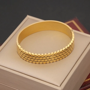 Dettaglio ravvicinato di un bracciale dorato con texture a tripla onda su portagioie