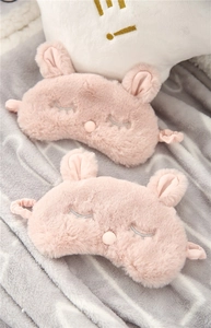 Close-up of pink plush bunny sleep masks with cute ears on a soft textured blanket