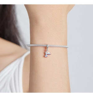 Close-up of a silver mesh bracelet featuring a delicate red enamel bird charm on wrist