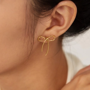 Elegant gold-tone bow stud earrings for women shown worn on a model's ear