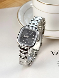 Silver square quartz watch with grey dial styled on magazine beside white tea cup
