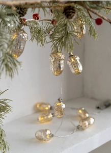 Detail of warm white LED acorn pinecone string lights on pine branches and white surface