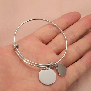 Close-up of polished silver stainless steel bangle with round and heart charms in palm