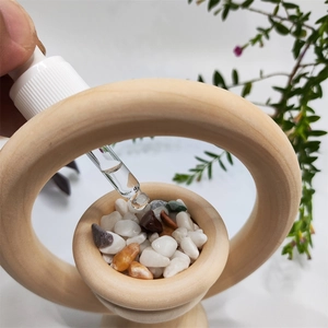 Detail of hand using a dropper to apply essential oils onto colorful stones in a wooden diffuser