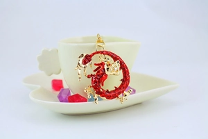 Detail of a red and gold dragon-shaped metal keychain hanging on a white ceramic cup