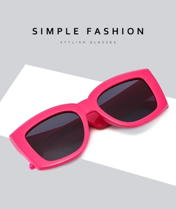 Detailed close-up of pink oversized square sunglasses with dark tinted lenses on grey