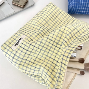 Detail of plaid toiletry bag with woven label showing cosmetic brushes and storage capacity