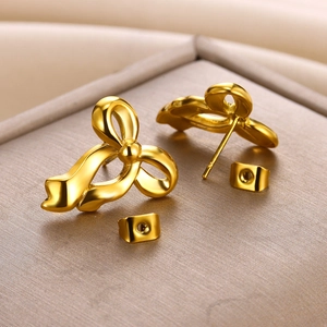 Detailed view of polished 18K gold-plated bow earrings on a textured metallic display