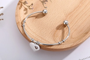 Detailed view of silver stainless steel open bangle with hollow heart charm on wood