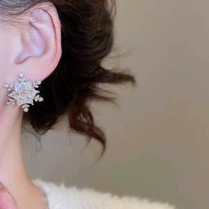 Close-up of sparkling snowflake earrings with zircon inlay on model's ear
