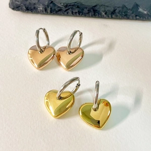 Detailed view of high-polished gold and rose gold heart hoop earrings on textured background