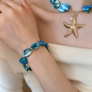 Detail of starfish charm and pearl necklace with blue shell stone on a model's neck