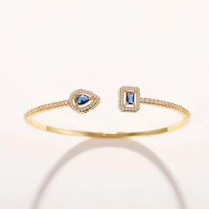 Detail of gold open bracelet with blue pear-cut and rectangular gemstones