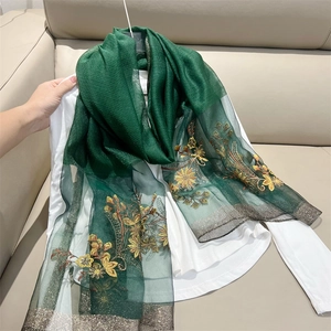 Dark green sheer scarf with gold floral embroidery on white blouse against beige background