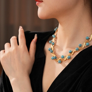 Close-up of vintage gold leaf necklace with turquoise beads and small rhinestones on a model