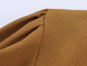 Detailed macro view of the pleated shoulder seam on a brown textured crepe fabric top