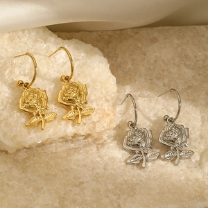 Detailed view of rose-shaped gold and silver earrings on a silk background