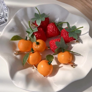 Detailed view of cute strawberry and orange fruit hair clips in a white ceramic bowl