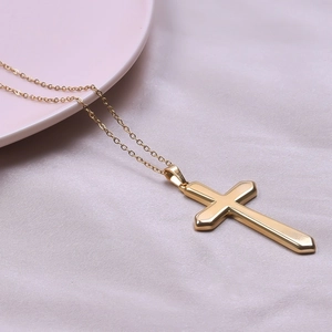 Detailed view of a polished 18k gold-plated cross pendant on a silk fabric background