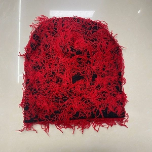 Detailed close-up of red and black knit beanie with distressed fringe texture on tiles