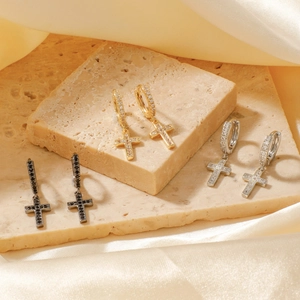 Close-up of cross earrings in gold, silver, and black finishes with inlaid cubic zirconia