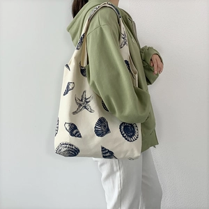 Detailed view of white canvas tote bag with blue seashell pattern on model
