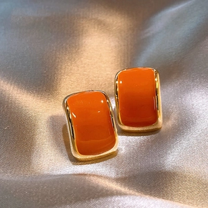 Elegant orange square stud earrings with gold metal frame on silk fabric background