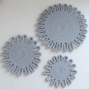 Detail of three gray woven cotton heat resistant mats in sunflower floral design