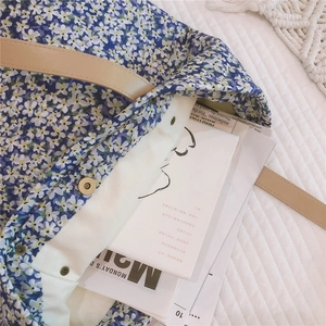 Detail of blue floral tote bag with leather straps and magnetic buckle on white fabric