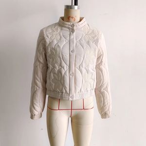 Detail of floral embroidery on a beige quilted jacket with stand-up collar and button closure