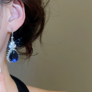 Close-up of elegant silver drop earrings with dark blue gemstone and white zircon accents