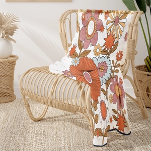 Retro floral flannel blanket with warm orange and pink tones draped on a rattan chair