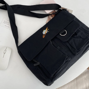 Close-up of black canvas crossbody bag featuring colorful planet embroidery and pockets