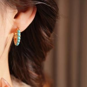 Close-up of model wearing 18k gold plated hoop earrings with turquoise beads detailing