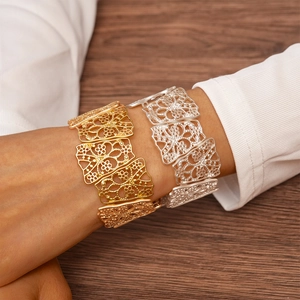 Detailed view of matte gold and silver hollow floral cuff bracelets on wooden background