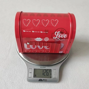 Detailed view of red tin mailbox gift box with heart pattern weighing 126.7g on scale