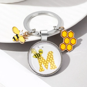 Macro shot of bee and honeycomb enamel charms with letter M on a silver keychain